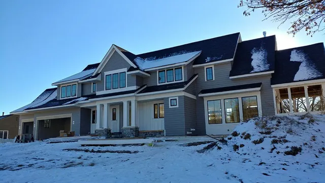 Large, two-story house with gray siding, snowy yard, and blue sky.