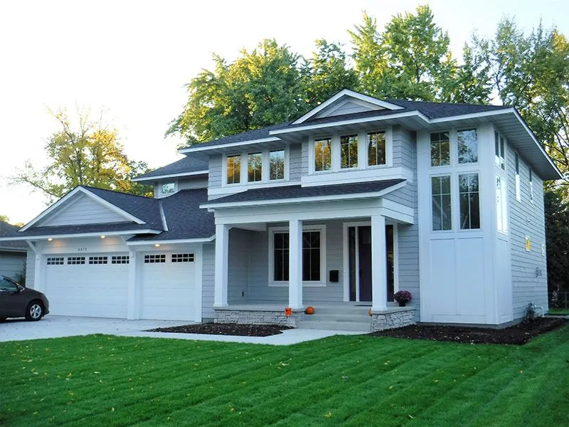 Two-story gray house with white trim, garage, front porch, and lush green lawn.