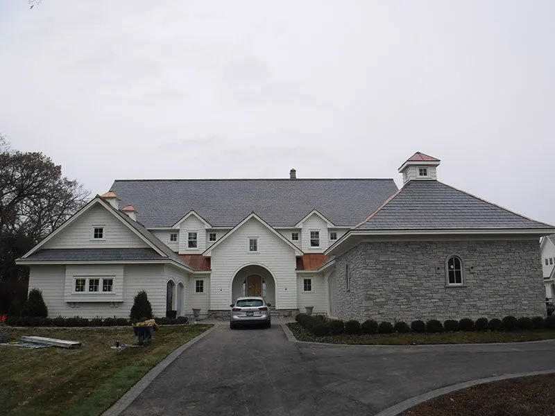 White building with dark roof, arched entrance, and stone addition; a car is parked in the driveway.