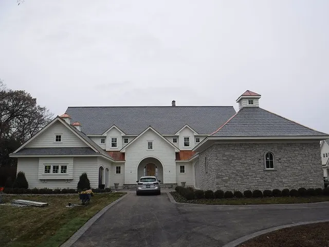 White building with dark roof, arched entrance, and stone addition; a car is parked in the driveway.