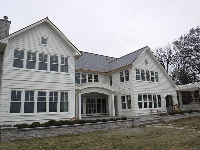 White two-story house with many windows and a stone wall at the base. Overcast day.